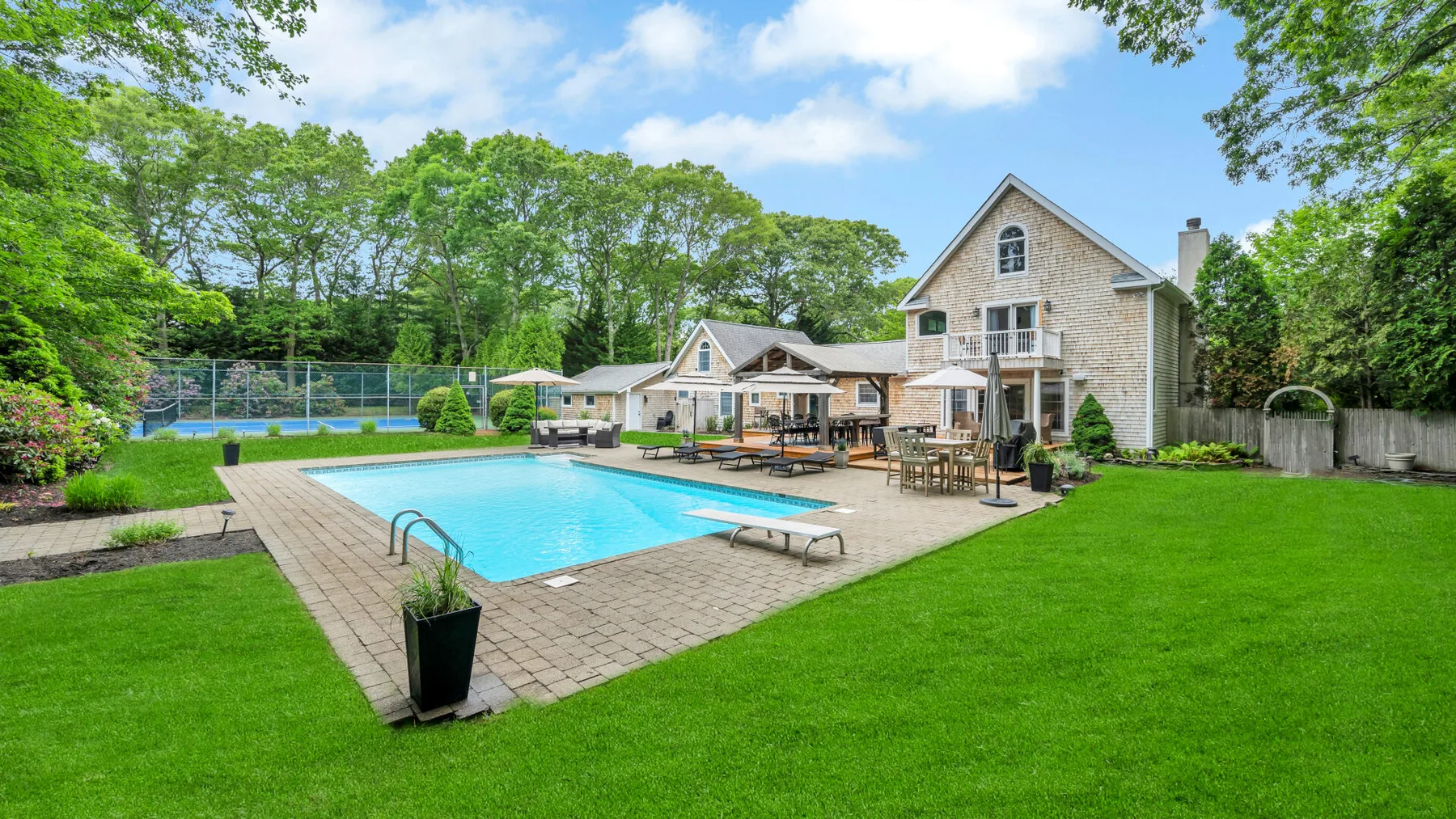 An outdoor swimming pool beside a house, with a patio and green lawn.