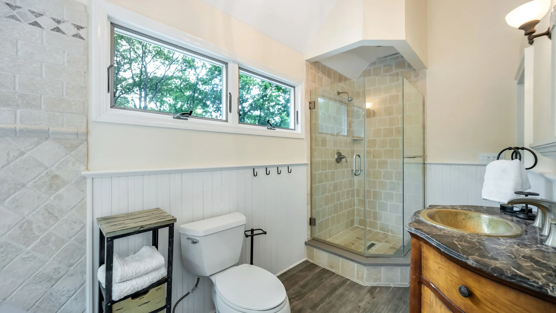 Un baño con ducha de vidrio, inodoro y lavabo bajo una ventana amplia.