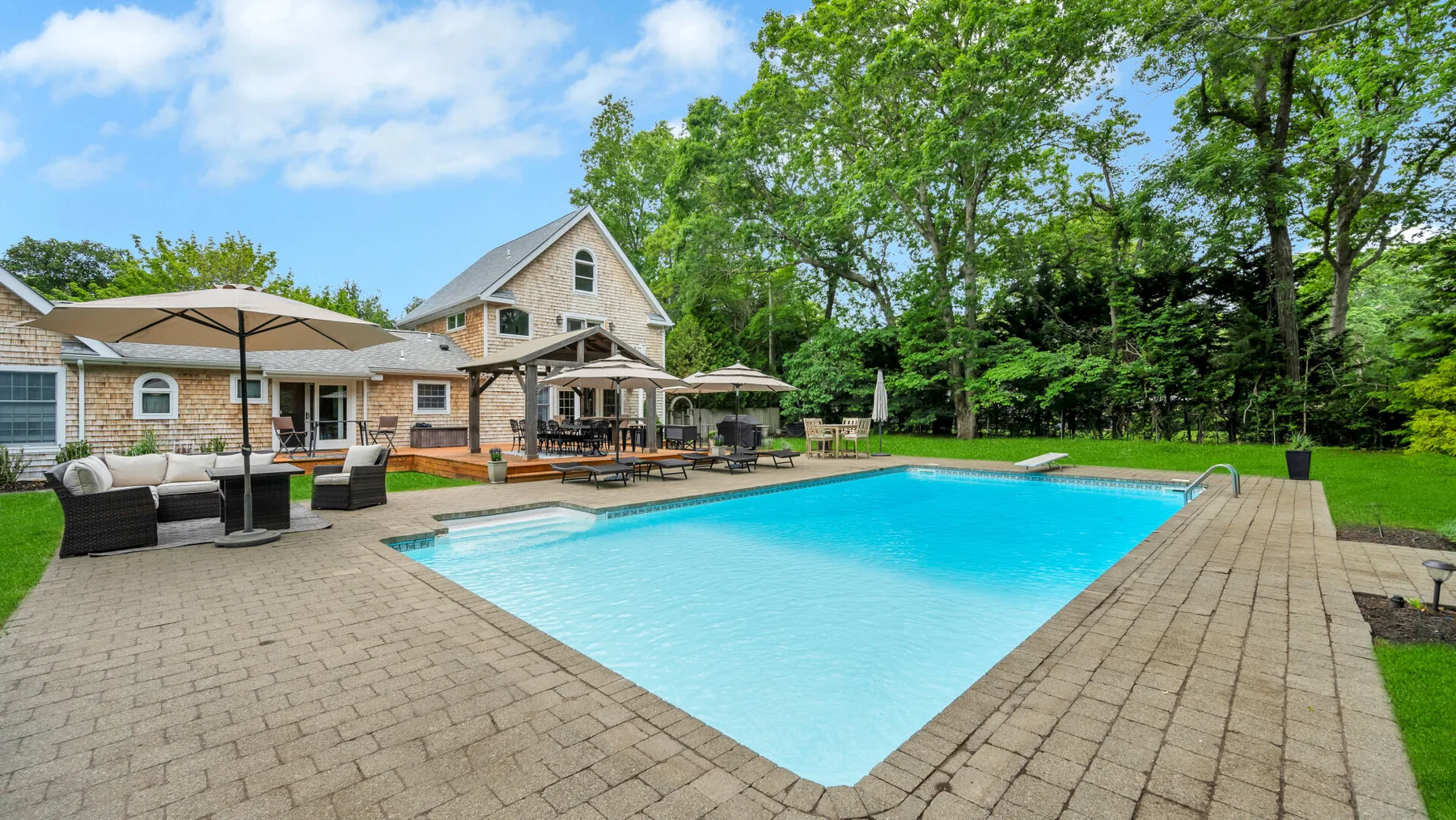 Una piscina junto a un patio pavimentado y una casa grande.