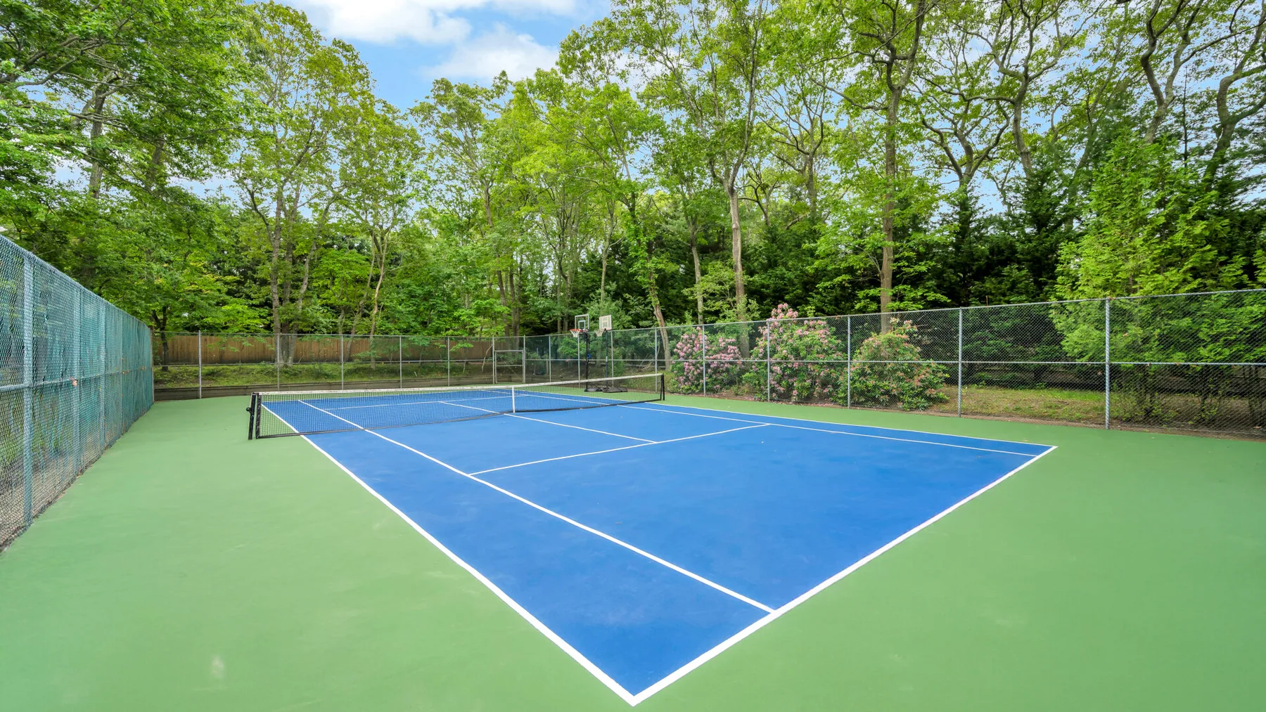 Una cancha de tenis al aire libre tiene una superficie azul rodeada de verde.
