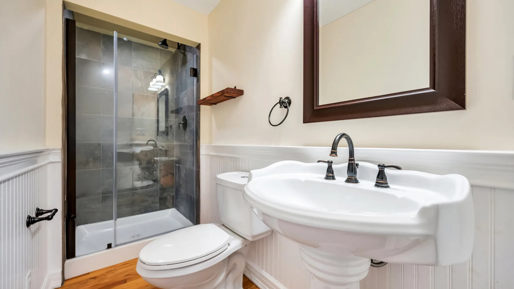 Un baño con ducha de vidrio, inodoro y lavabo con pedestal.