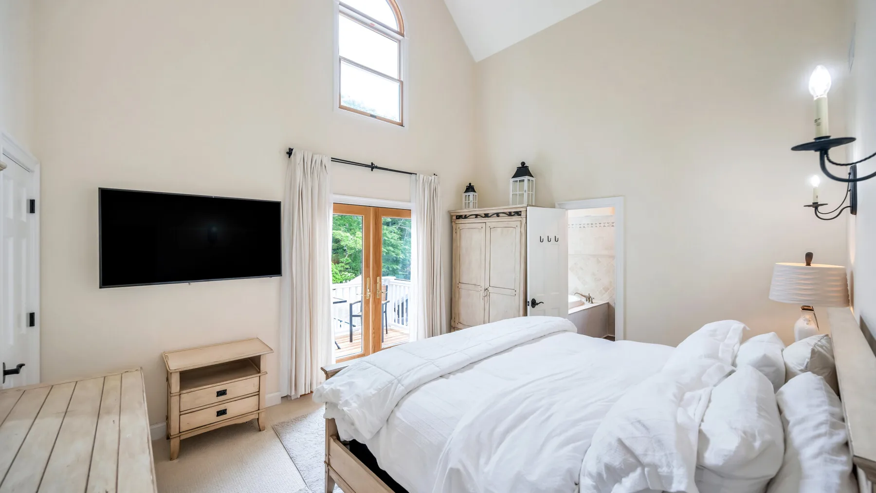Un dormitorio luminoso con una cama grande, un televisor y puertas que dan a un balcón.