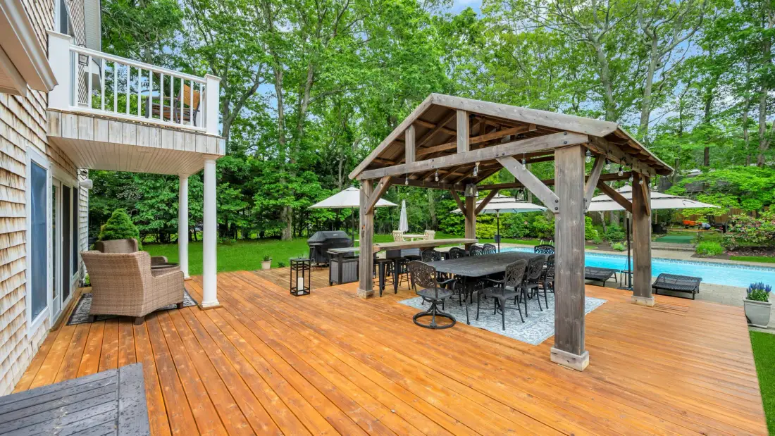Una terraza de madera tiene un comedor cubierto junto a una piscina.