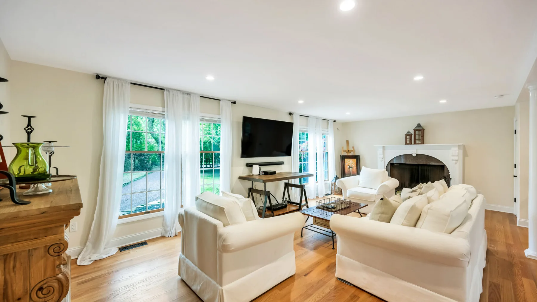 Una sala de estar luminosa con asientos claros, grandes ventanas y un televisor.
