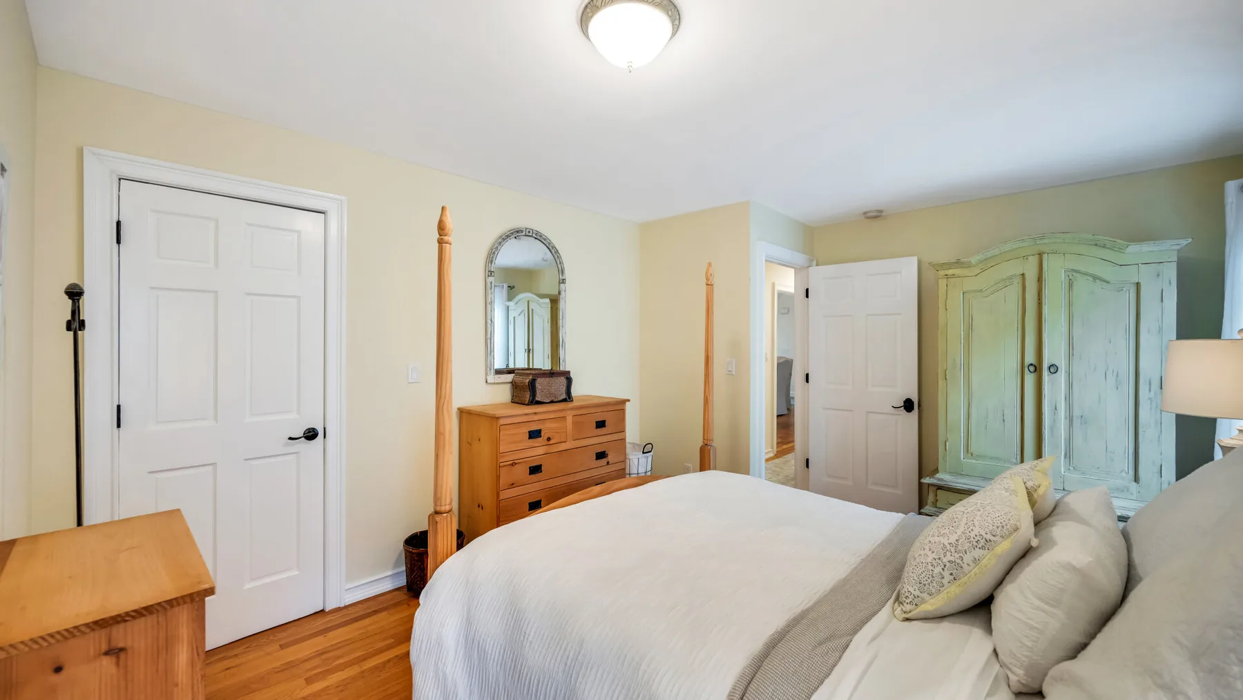 Un dormitorio con una cama, una cómoda de madera y un armario verde claro.
