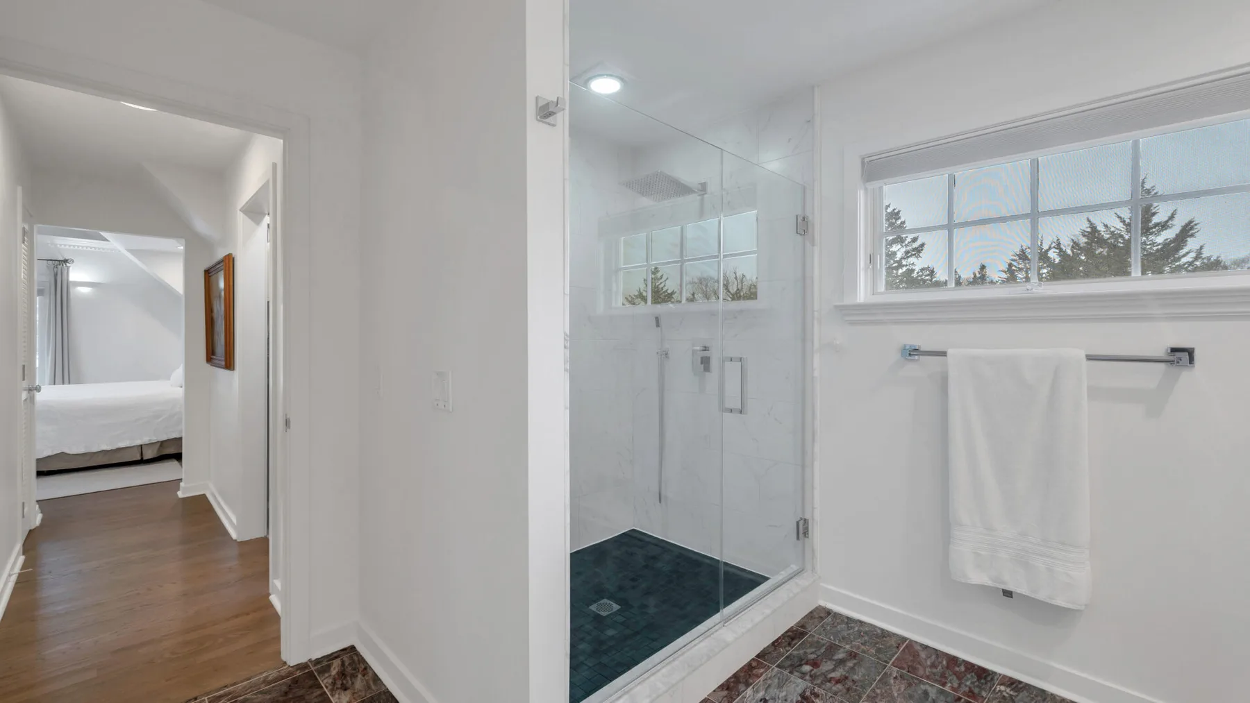 Un baño con una ducha de vidrio y una toalla colgada debajo de una ventana.