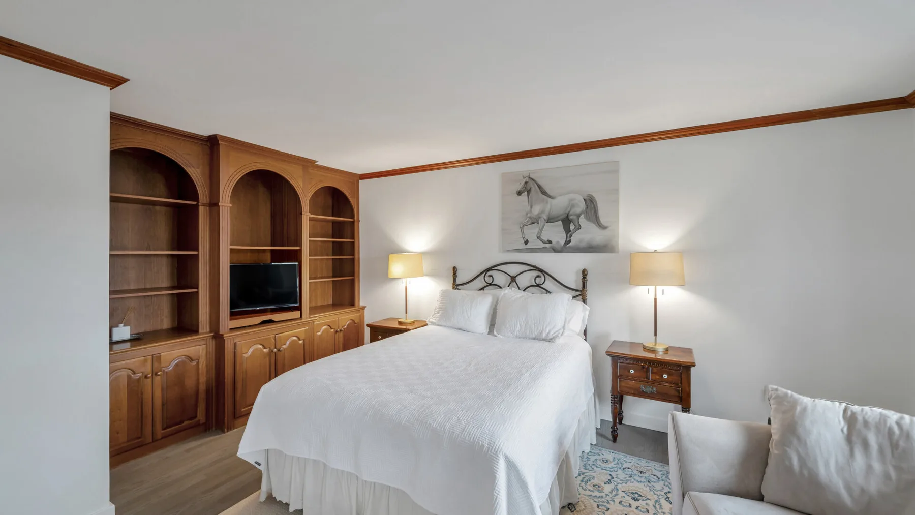 Un dormitorio con una cama bien tendida, armarios de madera y lámparas de noche.