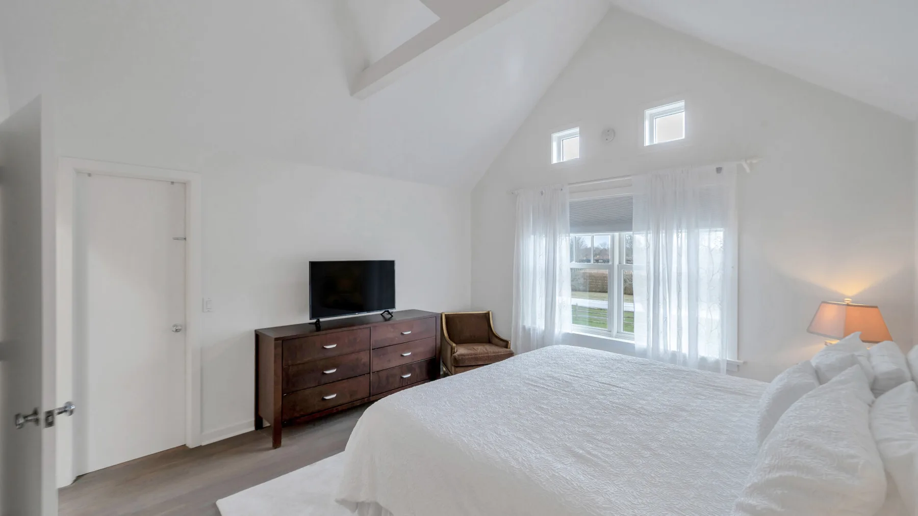 Un dormitorio luminoso con una cama, una cómoda y ventanas.