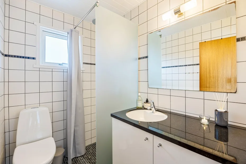 Un baño con azulejos, lavabo con mueble, espejo y cortina de ducha.