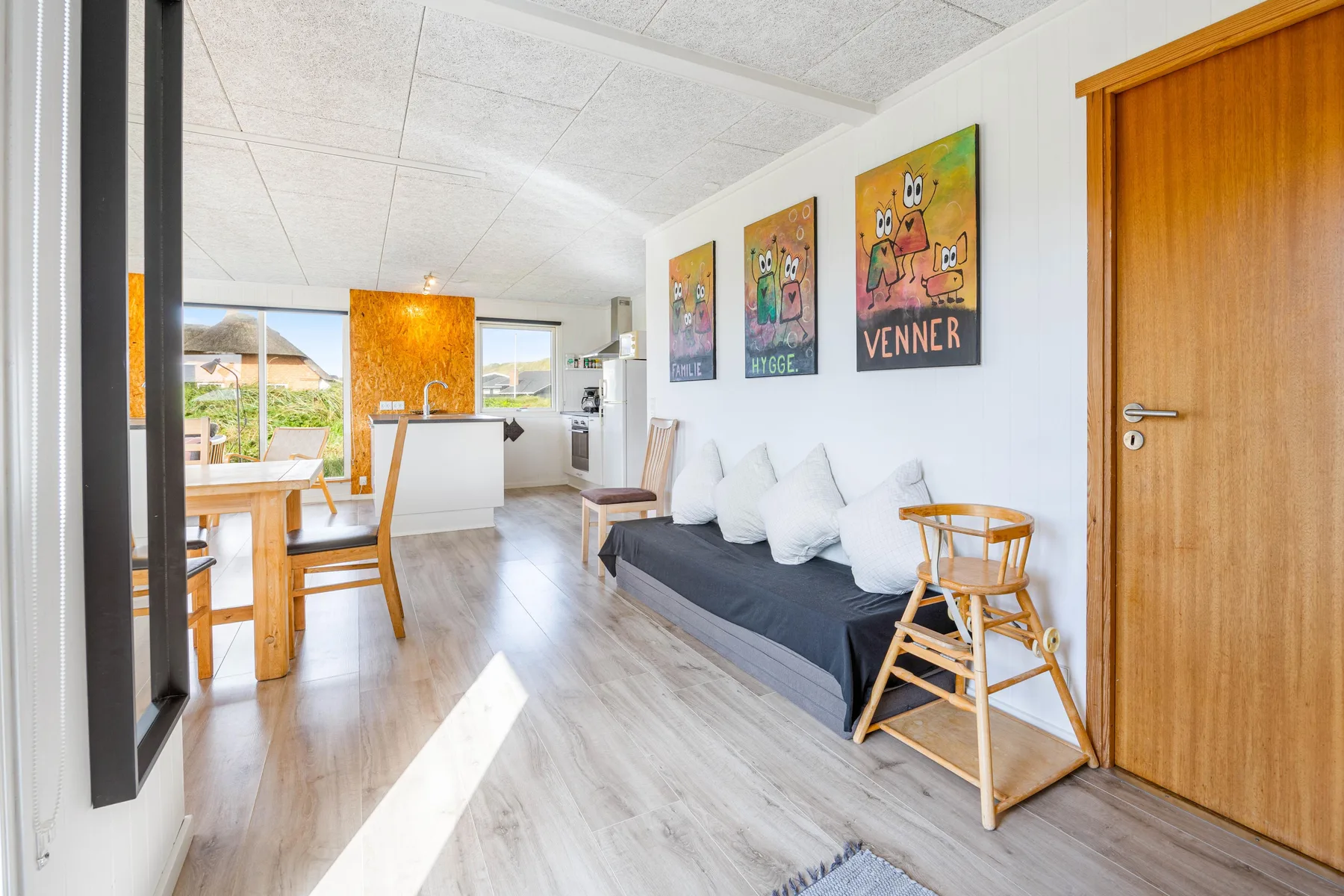 Una luminosa sala de estar y comedor con asientos, una mesa de madera y cuadros coloridos.