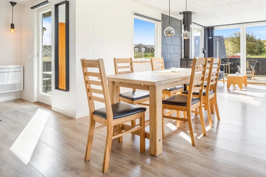 Un comedor luminoso con una mesa de madera y sillas junto a grandes ventanas.