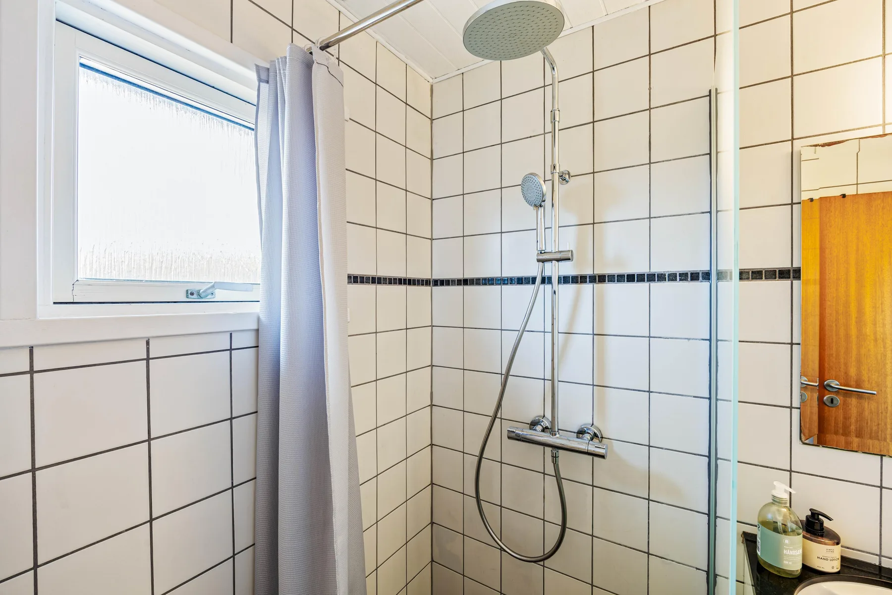 Una zona de ducha con azulejos, cortina y ventana.