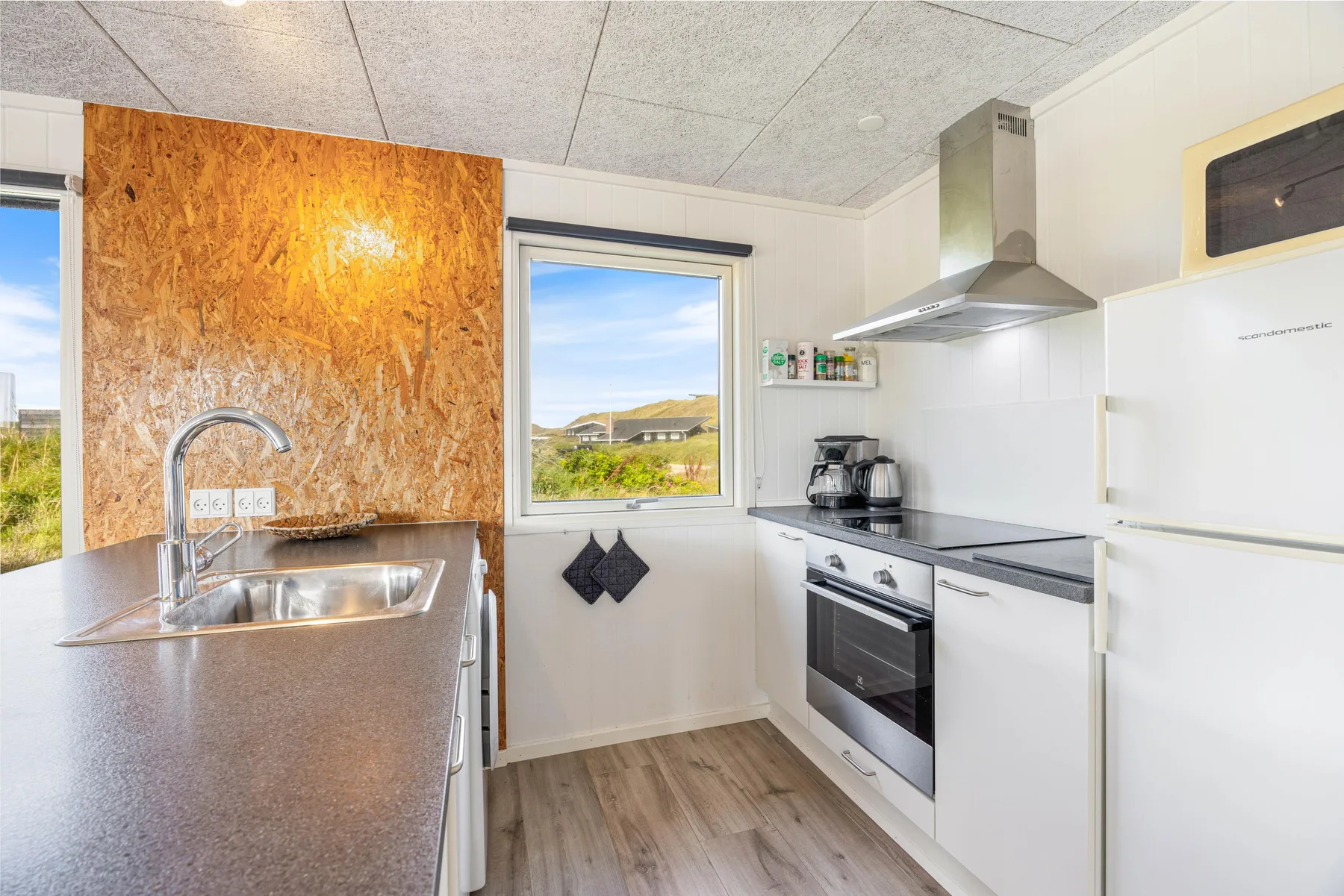 Una cocina luminosa con gabinetes blancos, fregadero y estufa bajo una campana extractora.
