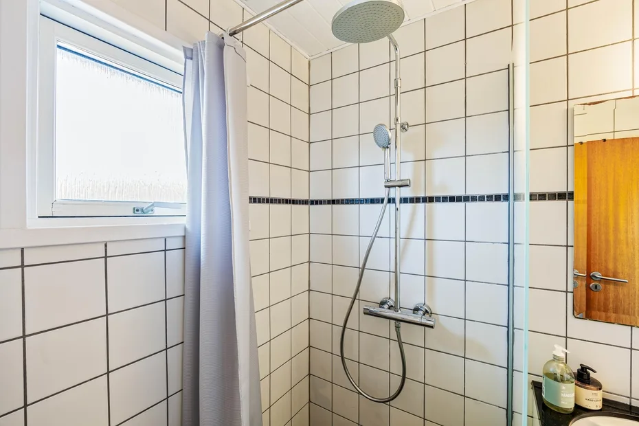 Zona de ducha con azulejos, una ducha de mano y una ventana.
