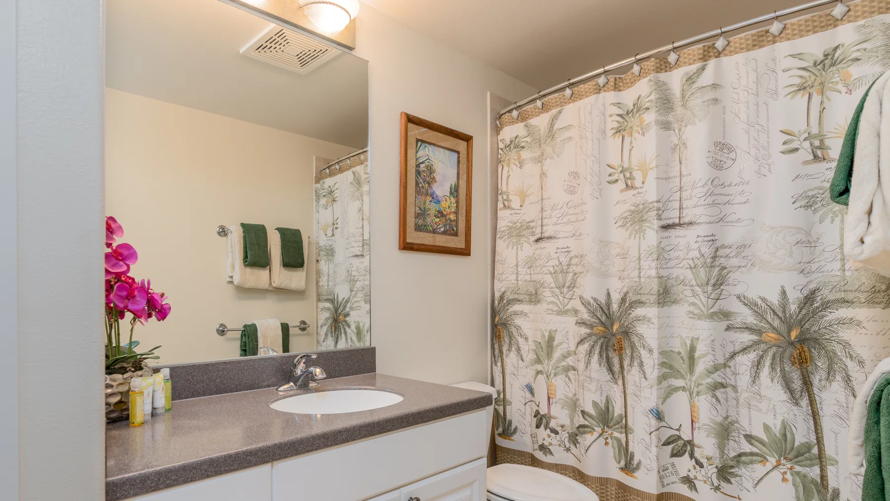Un lavabo de baño está junto a una cortina de ducha con un estampado de palmeras.