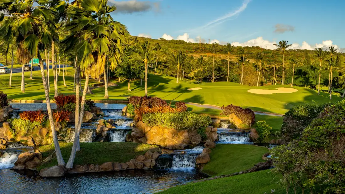 Un campo de golf ajardinado con palmeras, césped y un arroyo.