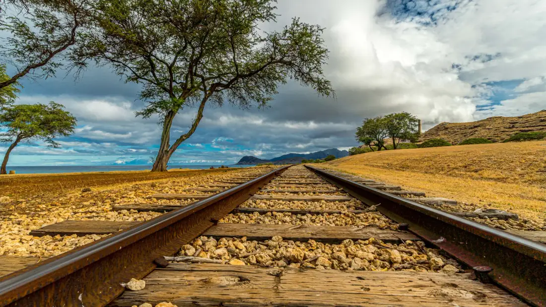 Una vía de tren atraviesa un paisaje seco y abierto bajo un cielo parcialmente nublado.