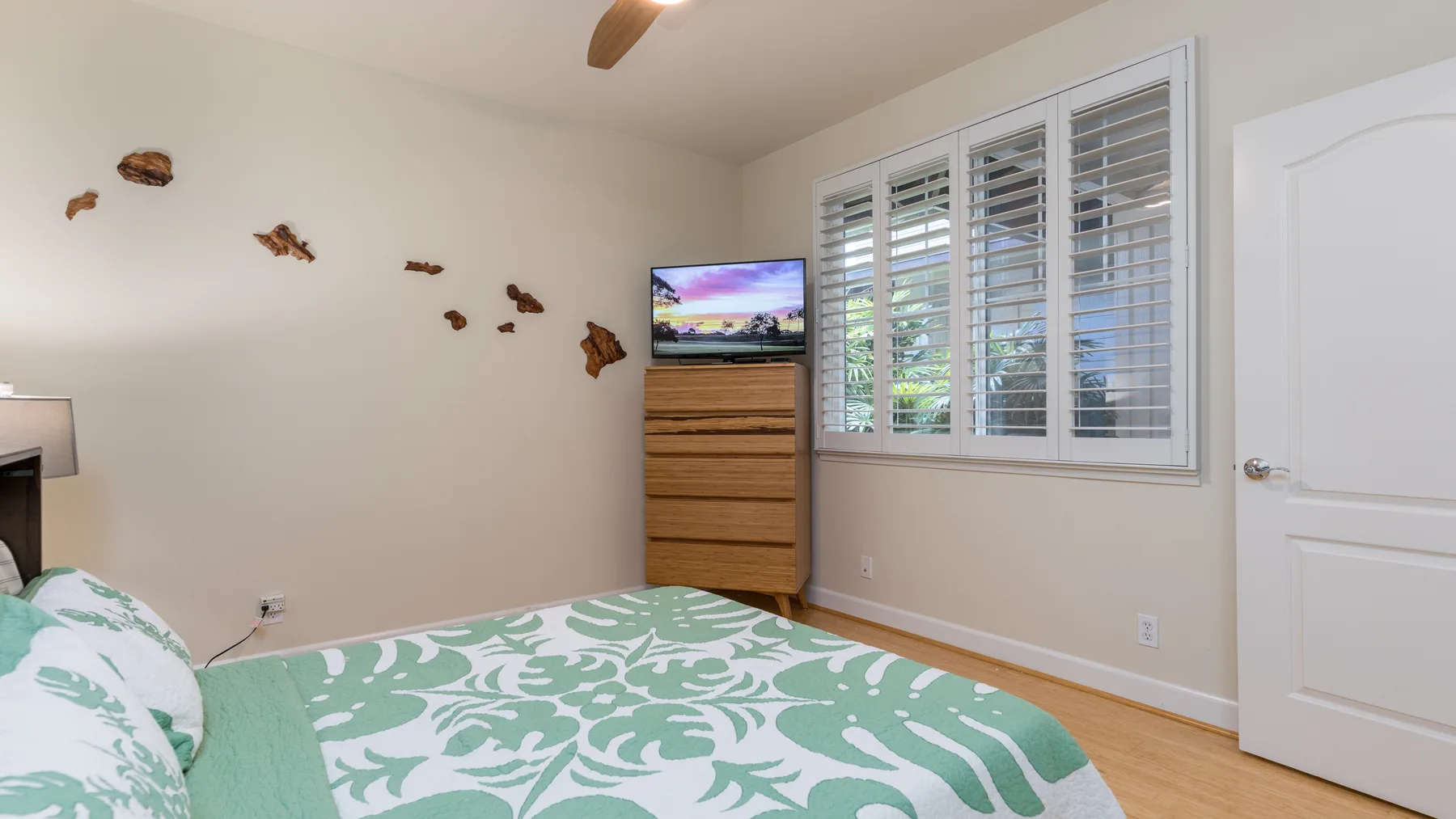 Un dormitorio con cama, cómoda y ventanas con contraventanas.