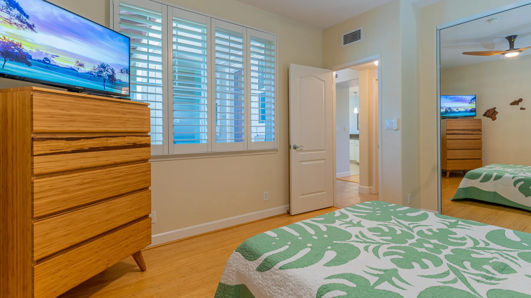 Un dormitorio con una colcha estampada verde y blanca y una cómoda de madera.