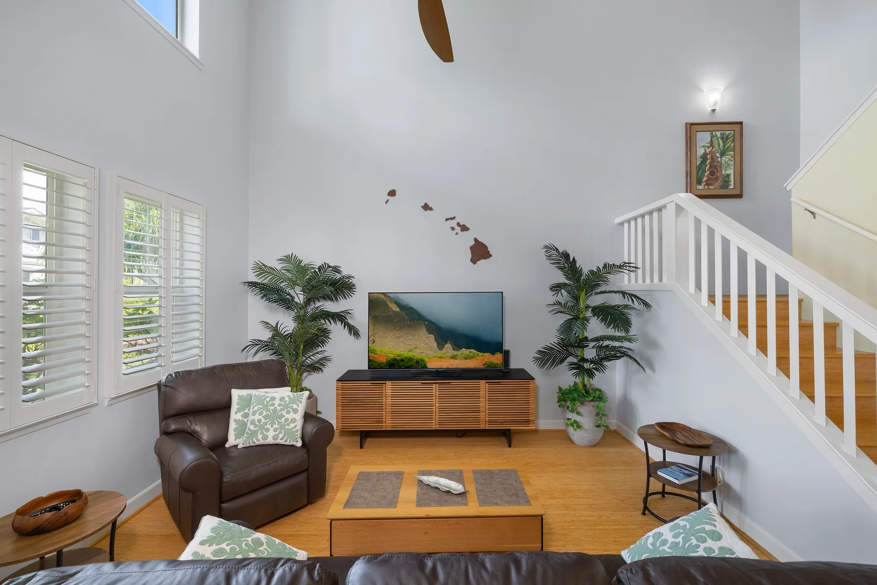 Una sala luminosa con televisor, asientos y una escalera.