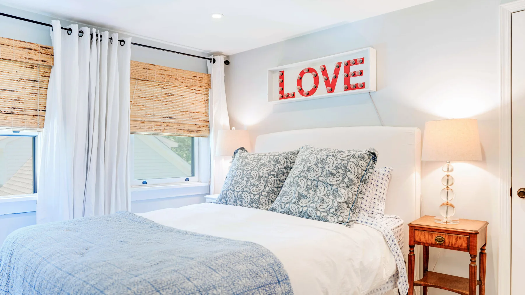 Un dormitorio luminoso con una cama bien tendida y un letrero rojo que dice «LOVE».