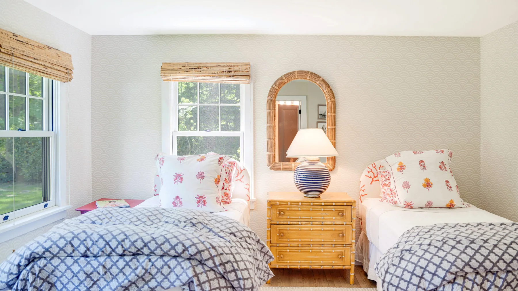 Un dormitorio luminoso con dos camas, ropa de cama estampada y una mesita de madera entre ellas.