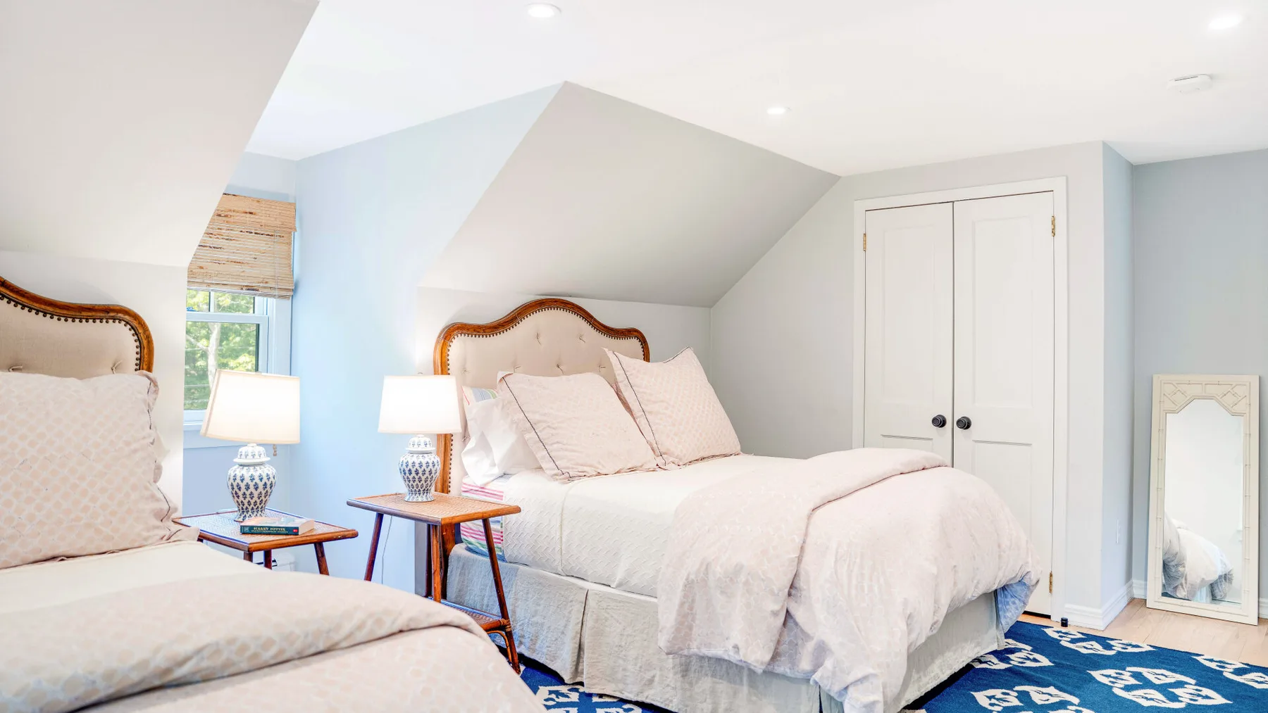 Un dormitorio abuhardillado luminoso con dos camas y una alfombra azul estampada.