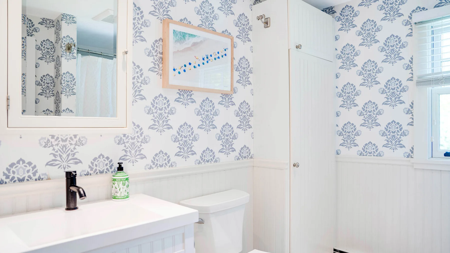 Un baño con lavabo, inodoro y papel tapiz floral azul.