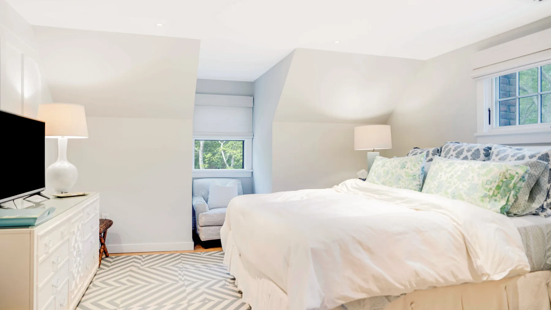 Un dormitorio luminoso con una cama, lámparas de mesita y una ventana.