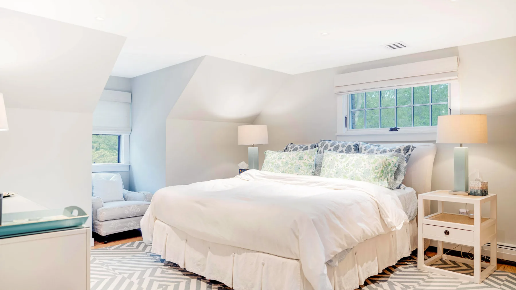 Un dormitorio luminoso con una cama bien tendida y una ventana con vistas a vegetación.