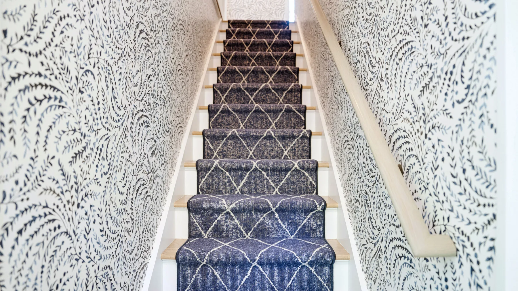 Una escalera alfombrada con papel tapiz estampado en ambas paredes.