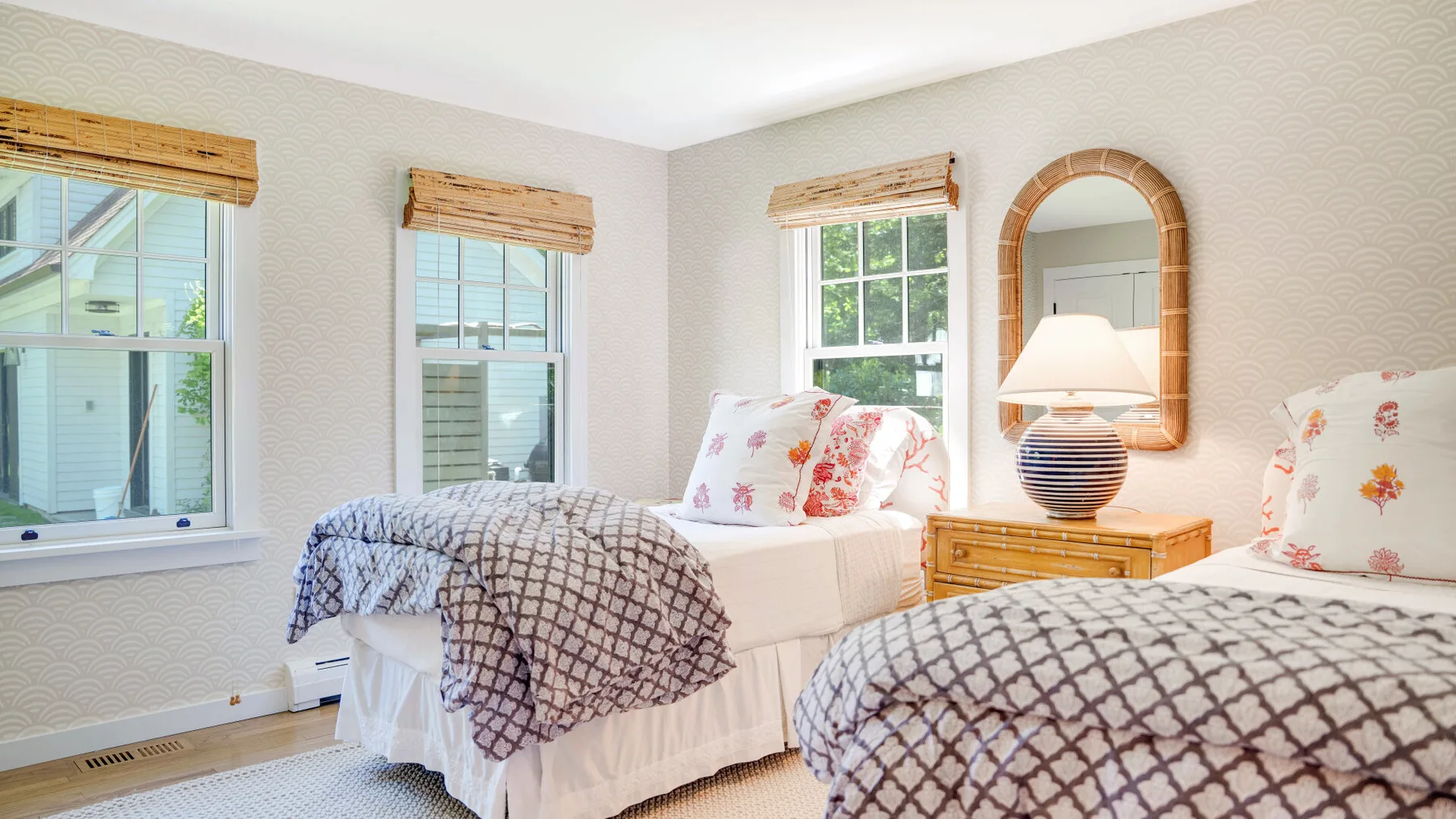 Un dormitorio luminoso con dos camas, ropa de cama estampada y ventanas con persianas tejidas.