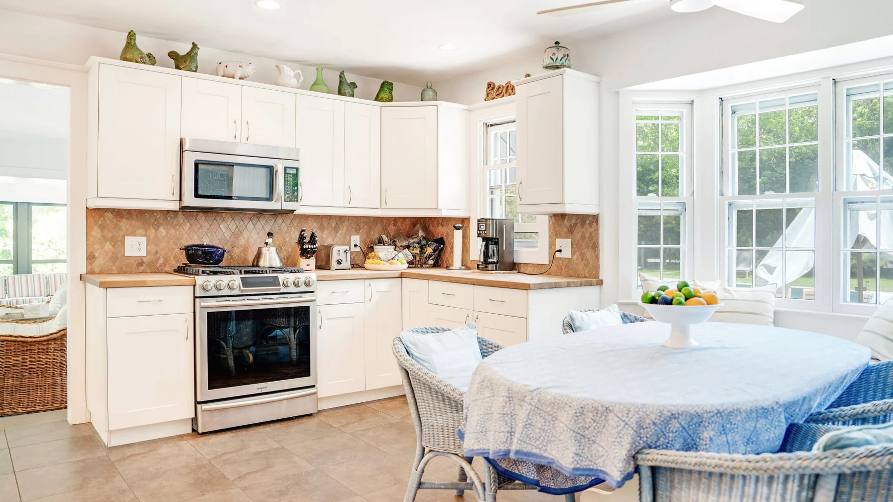 Una cocina luminosa con gabinetes blancos y una mesa redonda junto a grandes ventanas.