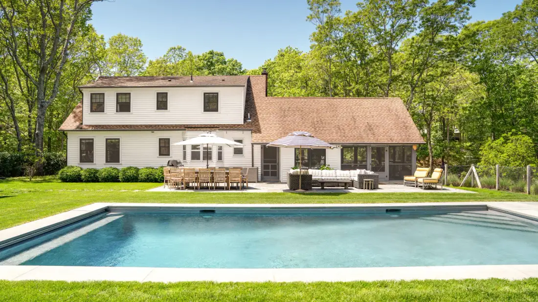 Una casa y una zona de estar al aire libre están junto a una piscina rectangular.