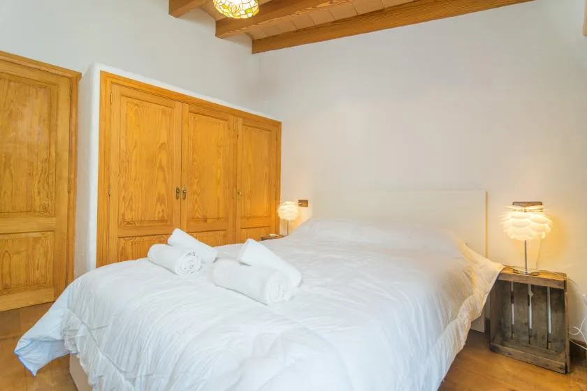 A bedroom with a bed dressed in white linens beside wooden cabinets.