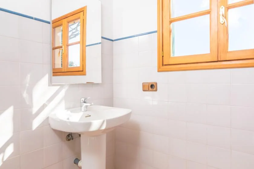 A bright bathroom with a pedestal sink and wooden-framed windows.