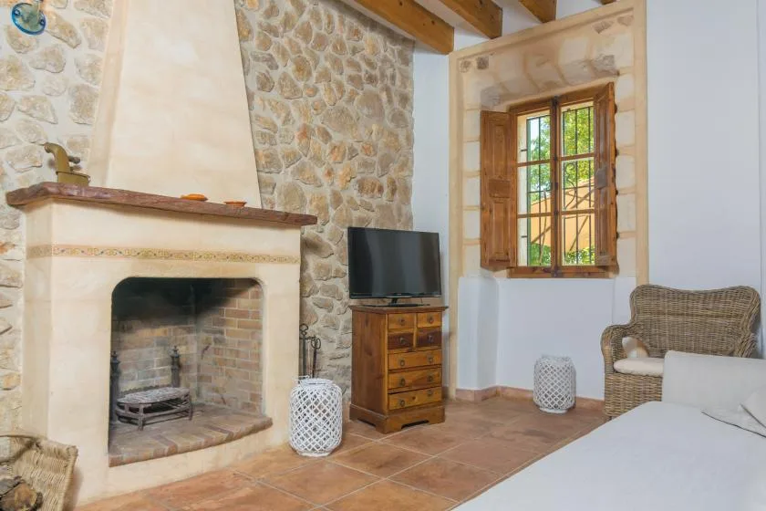 A rustic bedroom with a stone fireplace, television, and wooden window.