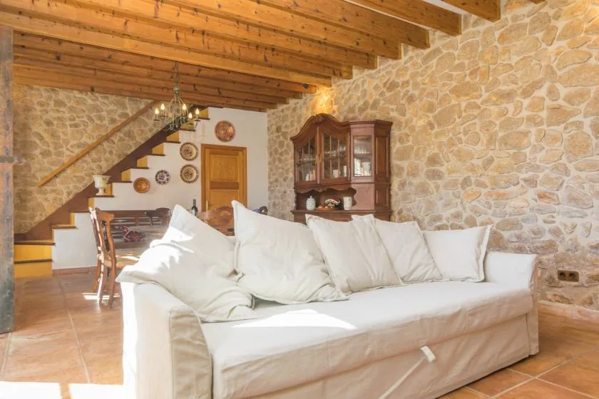 A living room with white seating, a stone wall, and exposed wooden ceiling beams.