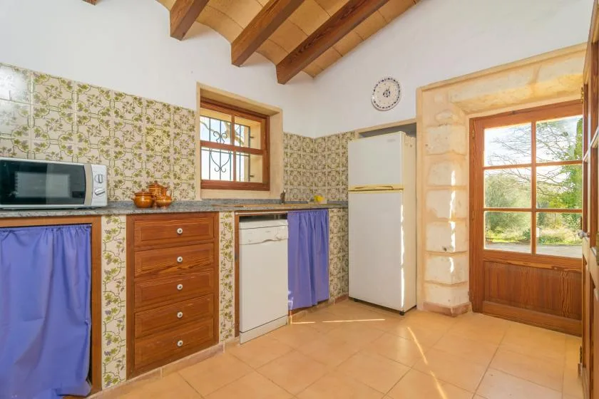 A tiled kitchen with a countertop, refrigerator, and wooden door.