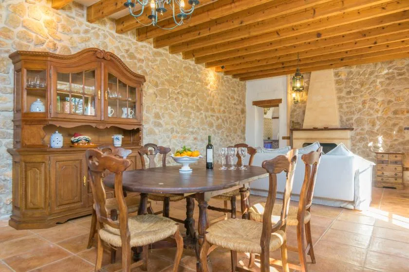 A rustic dining room with a wooden table and chairs beside a stone fireplace.