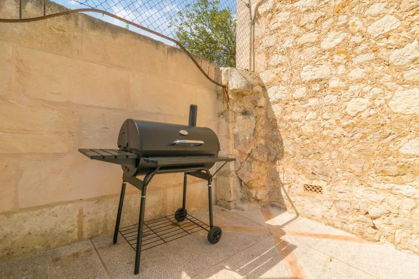 An outdoor barbecue grill stands beside a stone wall in a paved courtyard.