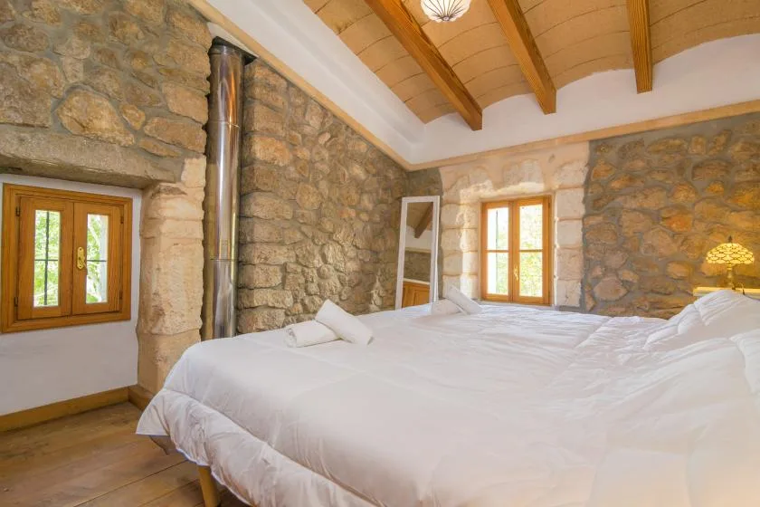 A bedroom with white bedding, stone walls, and wooden ceiling beams.