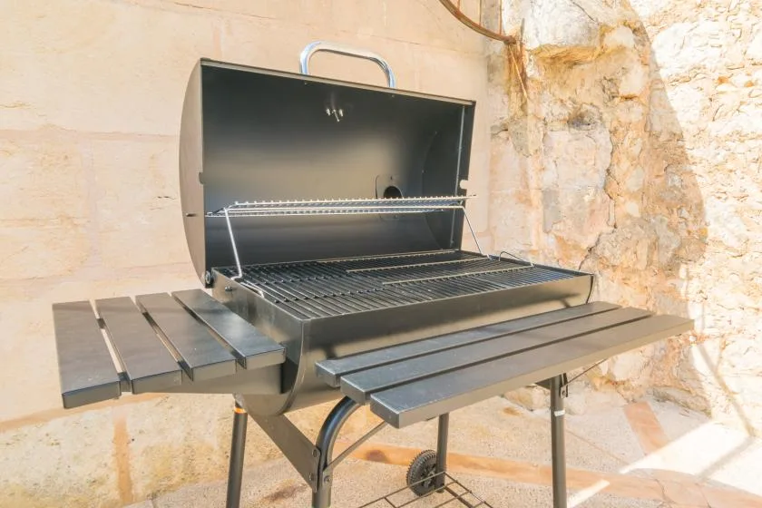 An open outdoor grill stands against a pale stone wall.