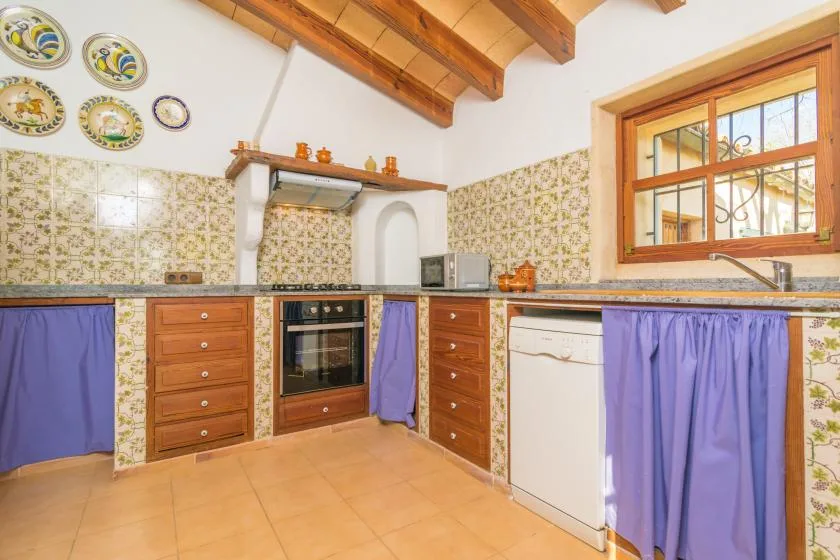 A tiled kitchen with wooden cabinets, an oven, and a window.