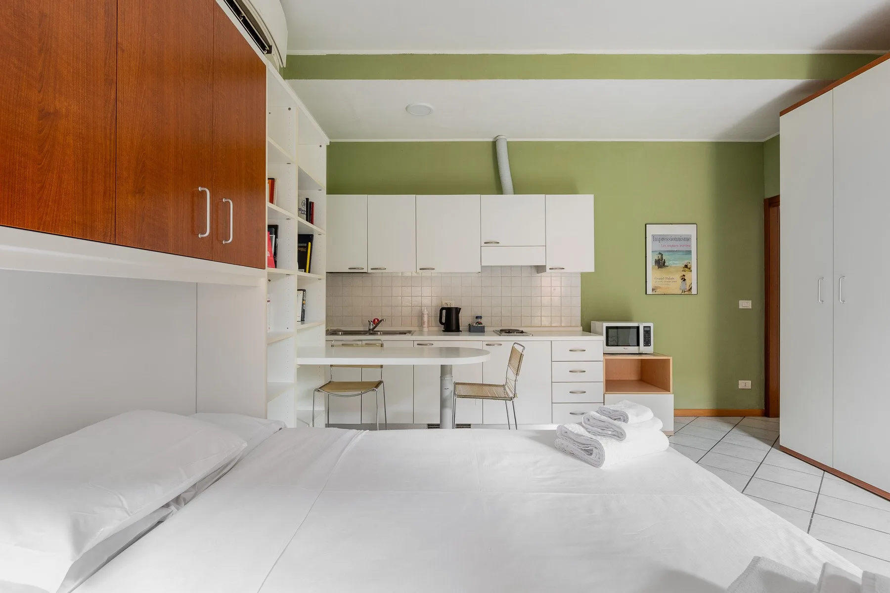 Un dormitorio con una cama frente a una pequeña cocina.