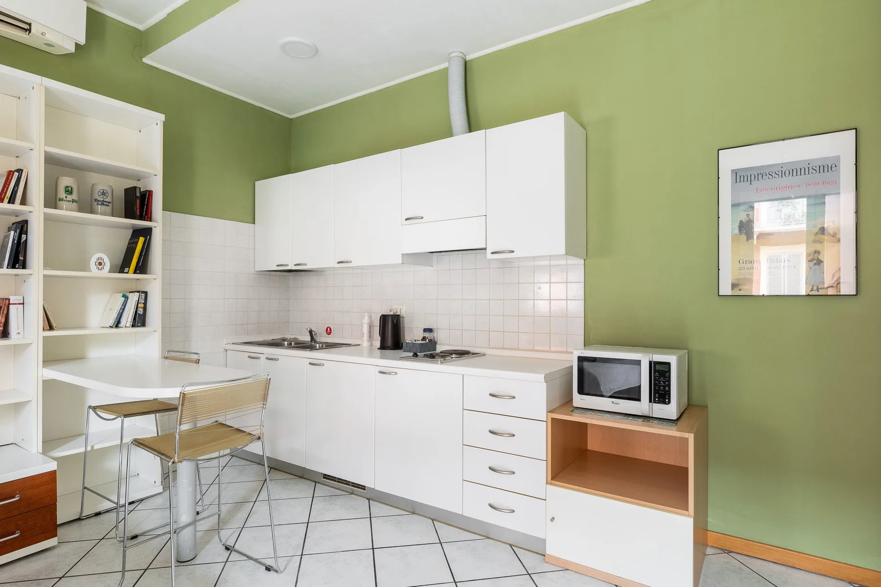 Una cocina compacta con gabinetes blancos, un salpicadero de azulejos y una pequeña mesa de comedor.