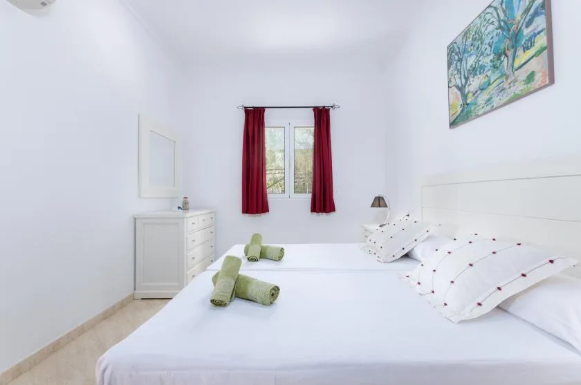 Un dormitorio luminoso con ropa de cama blanca, cortinas rojas y un cuadro colorido.