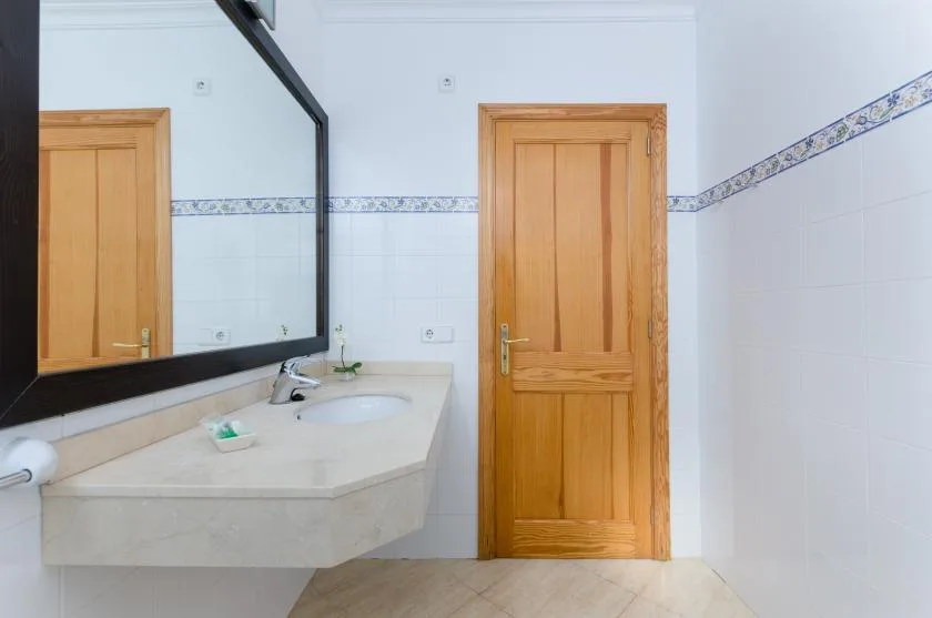 Un baño alicatado con lavabo, espejo grande y puerta de madera.