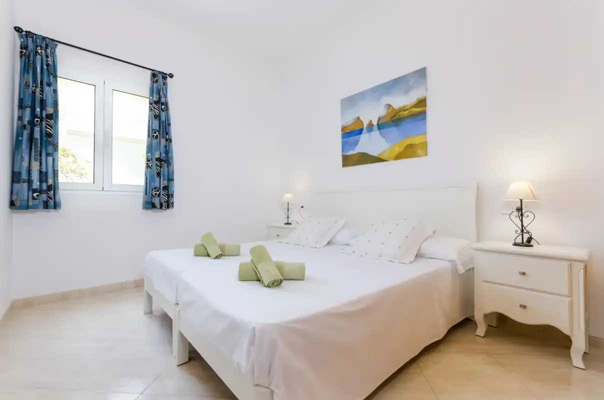 Un dormitorio con dos camas, mesillas y una ventana con cortinas azules.