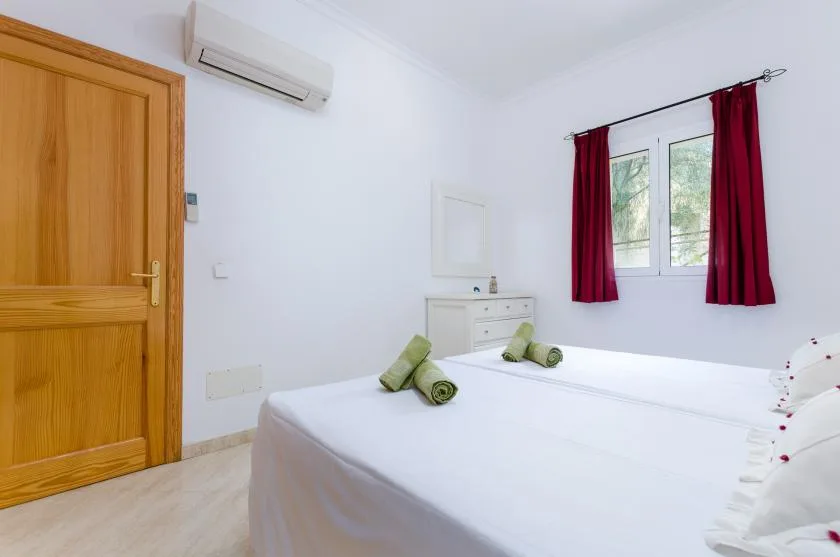 Un dormitorio luminoso con una cama blanca, una puerta de madera y una ventana con cortinas rojas.